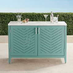 a sideboard with two drinks on it in front of a hedge and blue sky