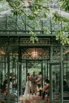 a bride and groom standing in front of a green gazebo surrounded by greenery