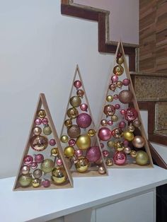 three wooden christmas trees on top of a white counter next to some stairs with ornaments hanging from them