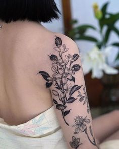 the back of a woman's shoulder with flowers and leaves tattooed on her arm