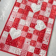 a red and white quilted table runner with heart appliqued on it