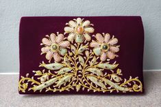 a purple purse with gold embroidered flowers on the front and sides, sitting on a table