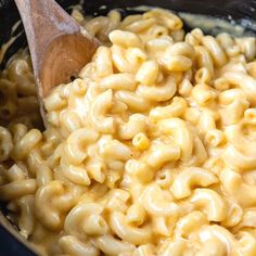 macaroni and cheese is being stirred with a wooden spoon in a slow cooker