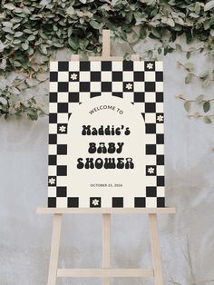 a welcome sign for a baby shower is displayed in front of a wall covered with greenery