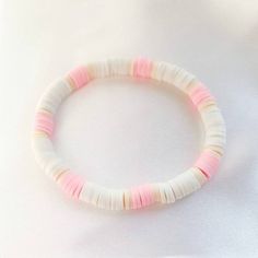 a pink and white beaded bracelet sitting on top of a white cloth covered table