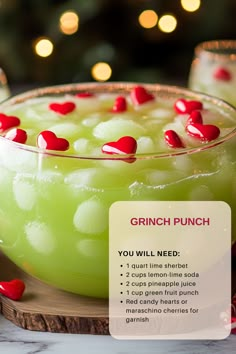 a green drink in a glass with red hearts on the rim and text that says grinch punch you will need