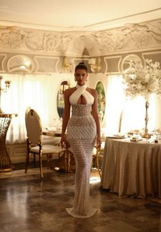 a woman in a white dress standing next to a table with gold chairs and tables