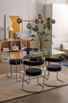 a glass dining table with four chairs and a plant in the middle, on a rug