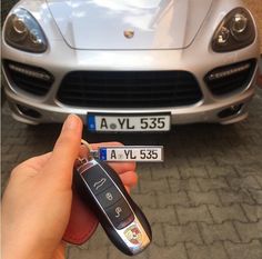 a hand holding a car key in front of a silver sports car with license plates