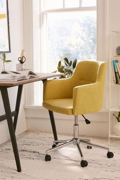 a yellow chair sitting in front of a window next to a desk with books on it