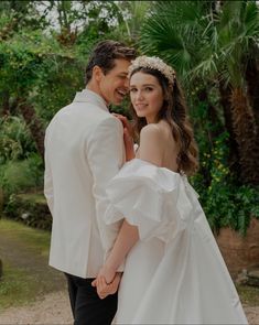 a man and woman in wedding attire standing next to each other on a dirt road