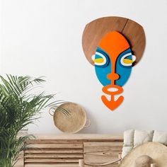 an orange and blue face is mounted on the wall next to a plant in a living room