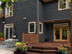 a house that is painted blue and has flowers on the front porch, with chairs around it