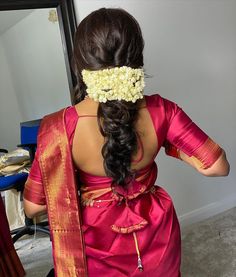 a woman with flowers in her hair is looking at herself in the mirror while wearing a pink saree