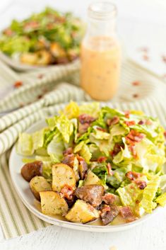 a salad on a plate with dressing next to it and a jar of dressing in the background