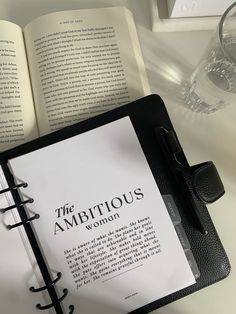 an open book sitting on top of a table next to a pen and glass filled with water