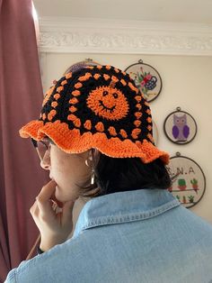 a woman wearing an orange and black crocheted sunhat in front of a window