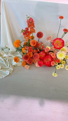 an arrangement of colorful flowers sitting on a white cloth covered table with drapes in the background