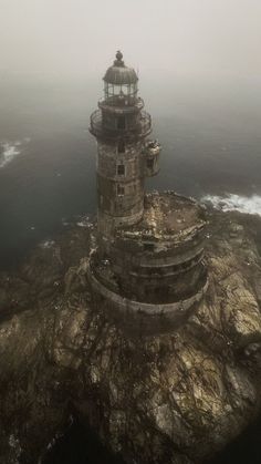 an aerial view of a lighthouse in the middle of the ocean on a foggy day