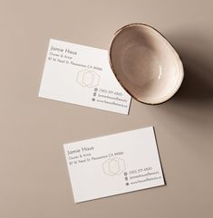 two business cards sitting on top of a white bowl next to a coffee cup and saucer