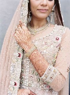 a woman wearing a bridal outfit and holding her hands up to her chest, smiling