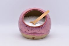 a pink and yellow ceramic container with a wooden spoon sticking out of it's side