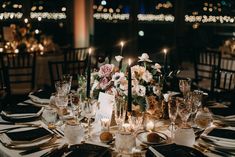 the table is set with silverware, candles and flower centerpieces on it