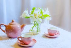 two cups and saucers on a table with flowers in a vase