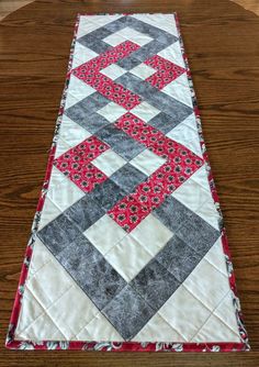 a quilted table runner with red and gray squares on it, sitting on a wooden surface