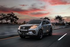 a silver suv driving down the road at sunset