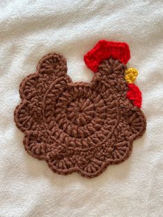 a crocheted chicken is laying on a white towel with red and yellow trim