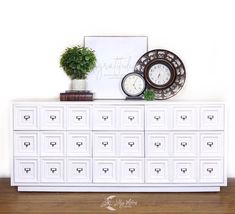 a white dresser with many drawers and clocks on top