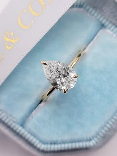 an engagement ring with a pear shaped diamond sits in a blue velvet box on the table