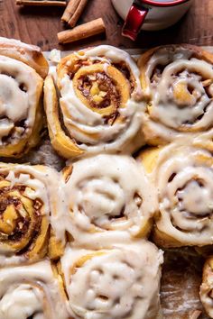 cinnamon rolls with icing sitting on top of a cutting board next to some cinnamon sticks