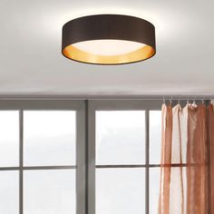 a round light fixture hanging from the ceiling above a window with curtains in front of it