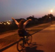 a person riding a bike down a street at night with their arms in the air