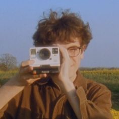 a man holding up a camera in front of his face while standing in a field