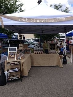 an outdoor market with tables and chairs under a white tent that says milk & honey grans farmers market visit