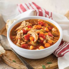 a bowl of chicken and bean soup on a wooden cutting board with a striped napkin