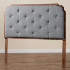 an upholstered headboard with wooden legs and buttons on the top, against a beige wall