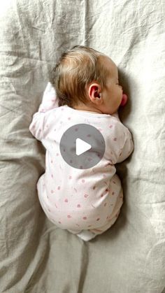 a baby laying on top of a bed next to a white sheet and pillow with a video play button