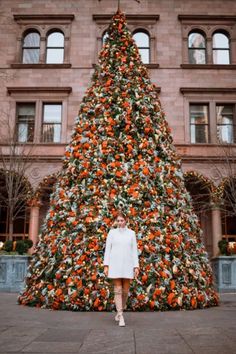 a woman standing in front of a large christmas tree with oranges on it's branches