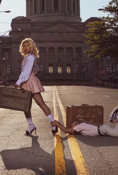 a woman is walking down the street with her suitcases in hand and another person laying on the ground