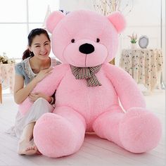 a woman sitting on the floor with a large pink teddy bear in front of her