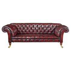 a red leather couch with gold legs and buttons on the arm, against a white background