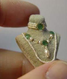 someone is holding a miniature ring with pearls and emeralds on it's side