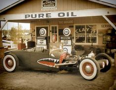 an old fashioned car is parked in front of a gas station with a shark's teeth painted on it