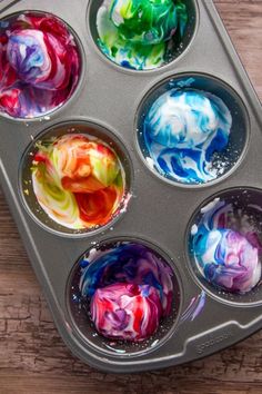 six muffin tins filled with different colored icing on top of a wooden table