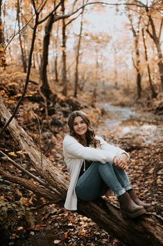 a woman sitting on top of a tree branch in the middle of an autumn forest