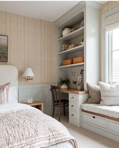 a bed sitting under a window next to a desk and book shelf in a bedroom